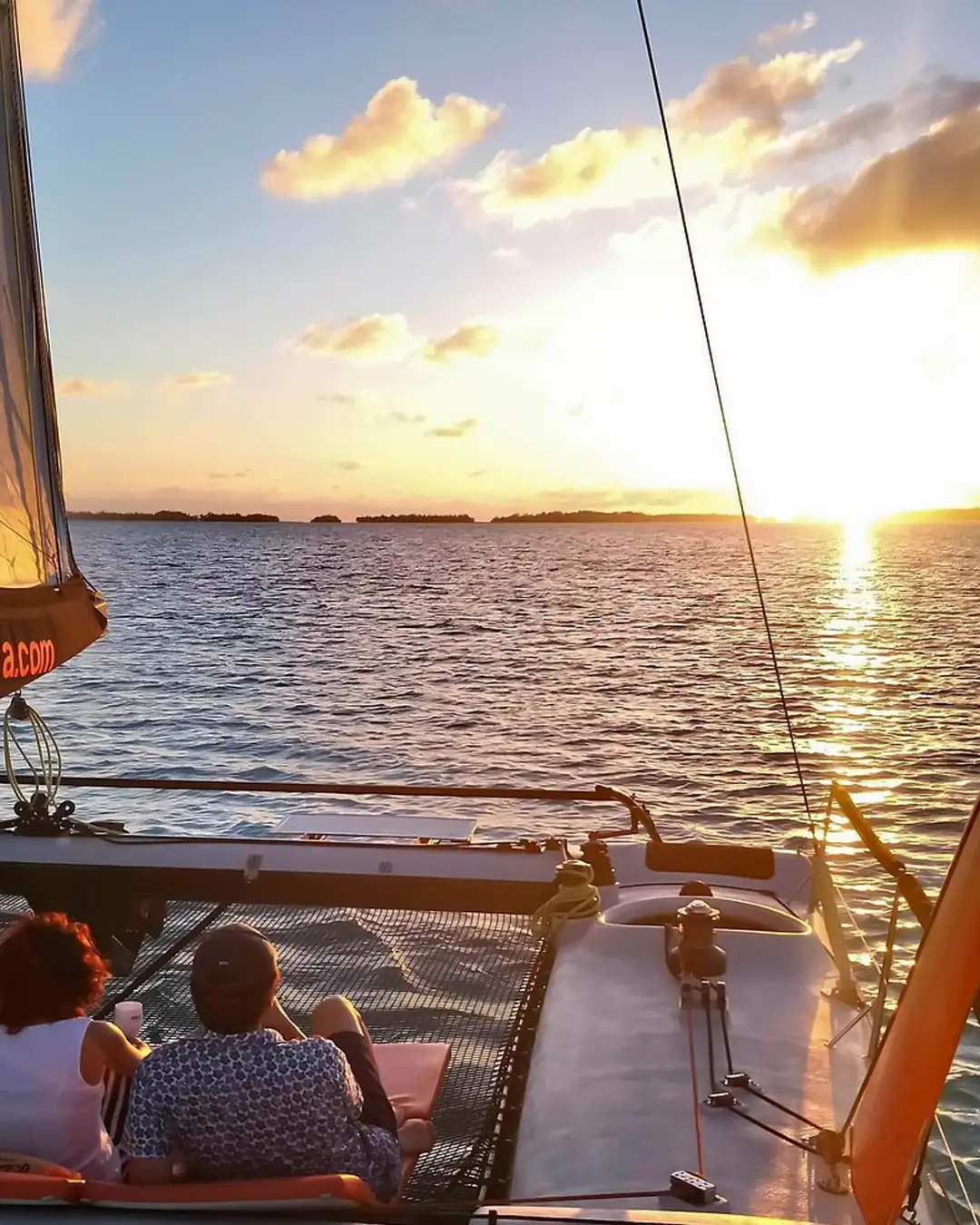 Couple watching the sunset in Bora Bora on the net of a private catamaran