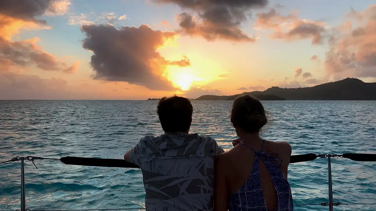 Two people sitting at the railing of a catamarn watching the sunset in Bora Bora